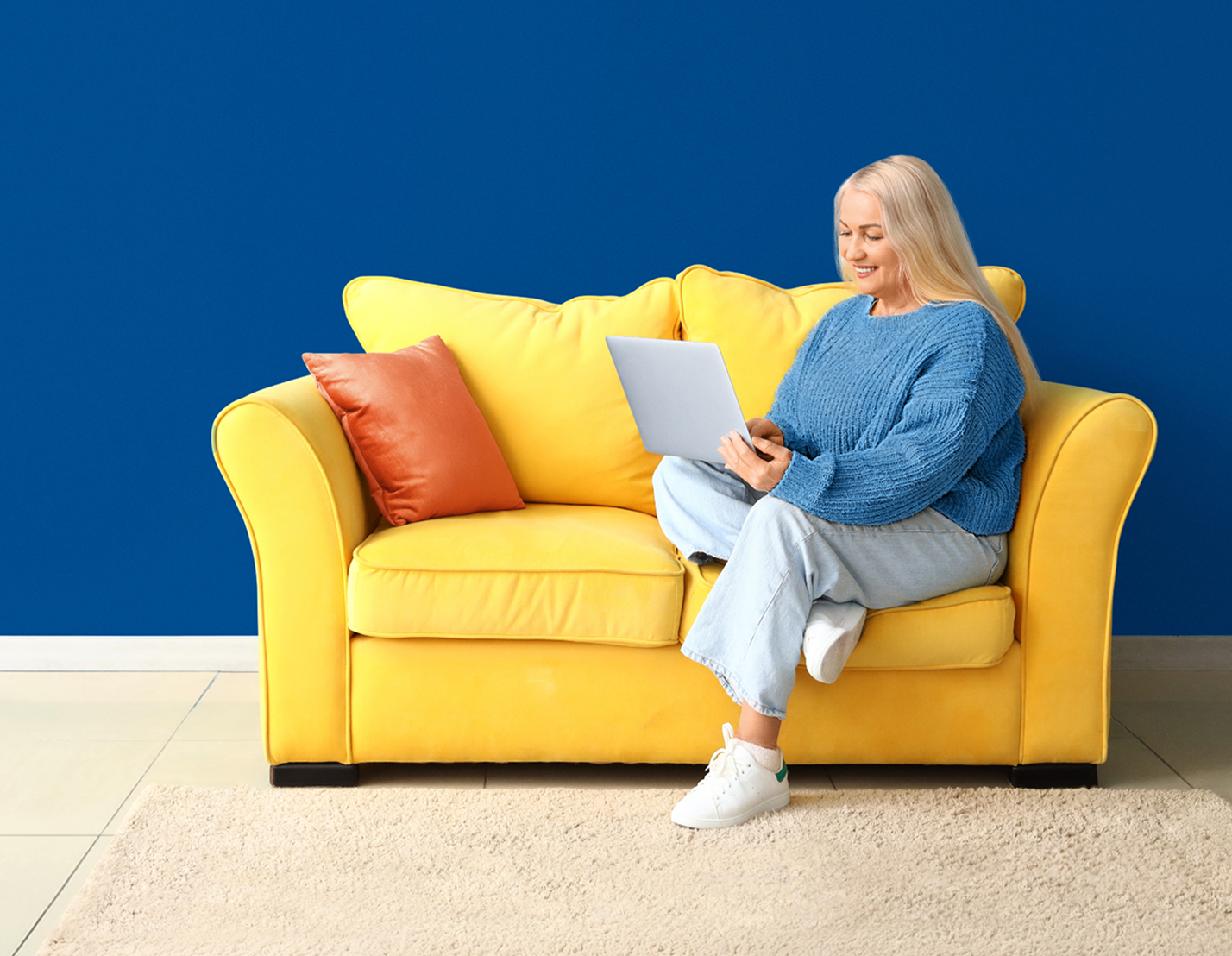 Woman sitting on a sofa using a laptop to explore My Compass Support for LISRAYA patients