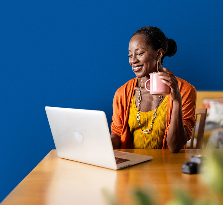 Woman drinking from a mug while using a laptop to learn about My Compass Support for LISRAYA patients